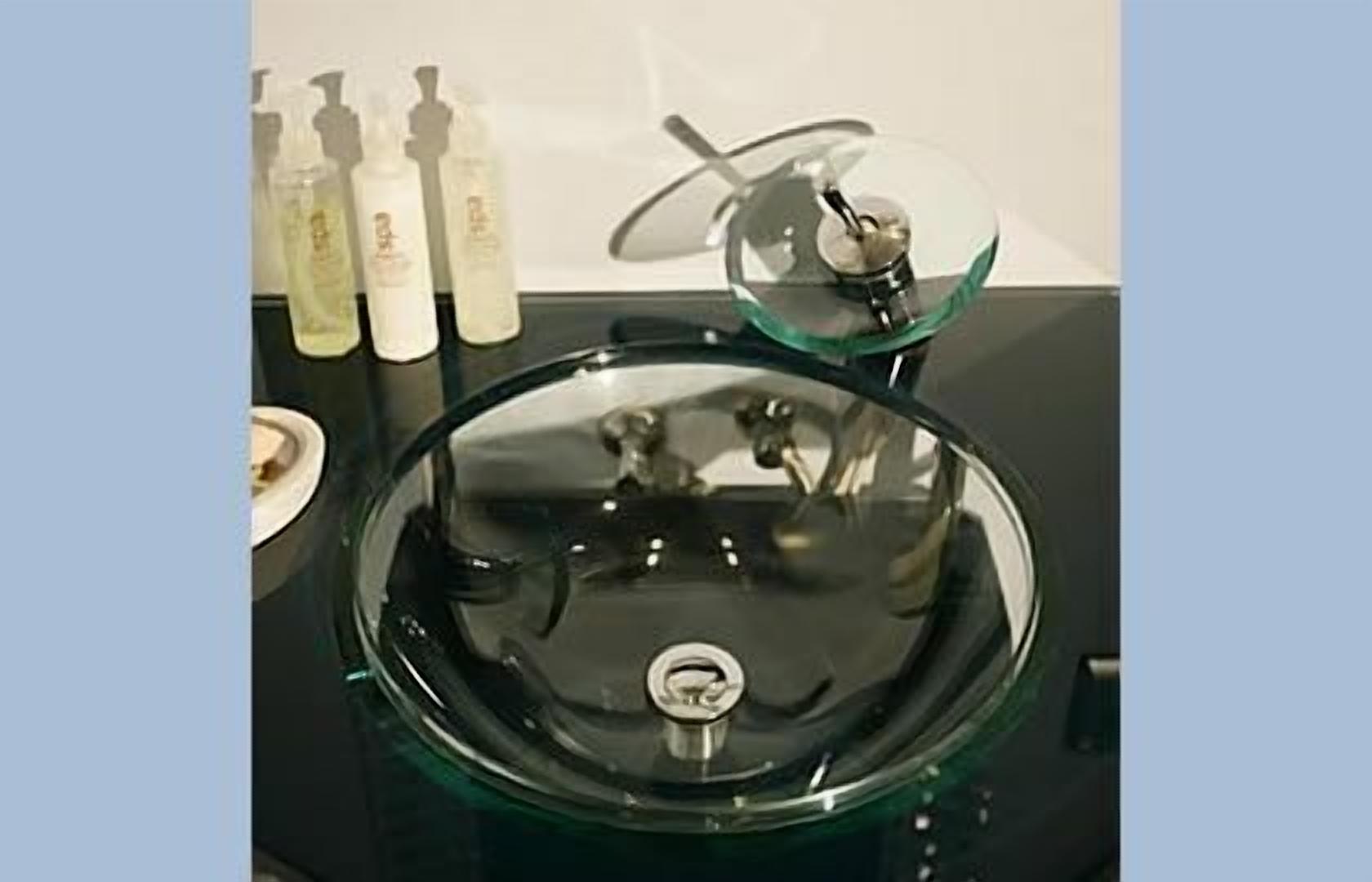 Une salle de bain dotée d’un lavabo moderne, d’une paroi en verre et de plusieurs flacons de produits de toilette disposés sur le comptoir.