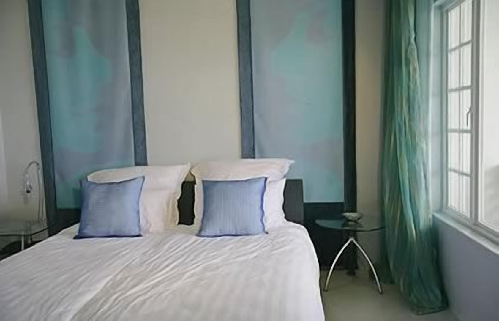 A hotel room with a bed, two pillows, a bedside table, a lamp, and a window with curtains.