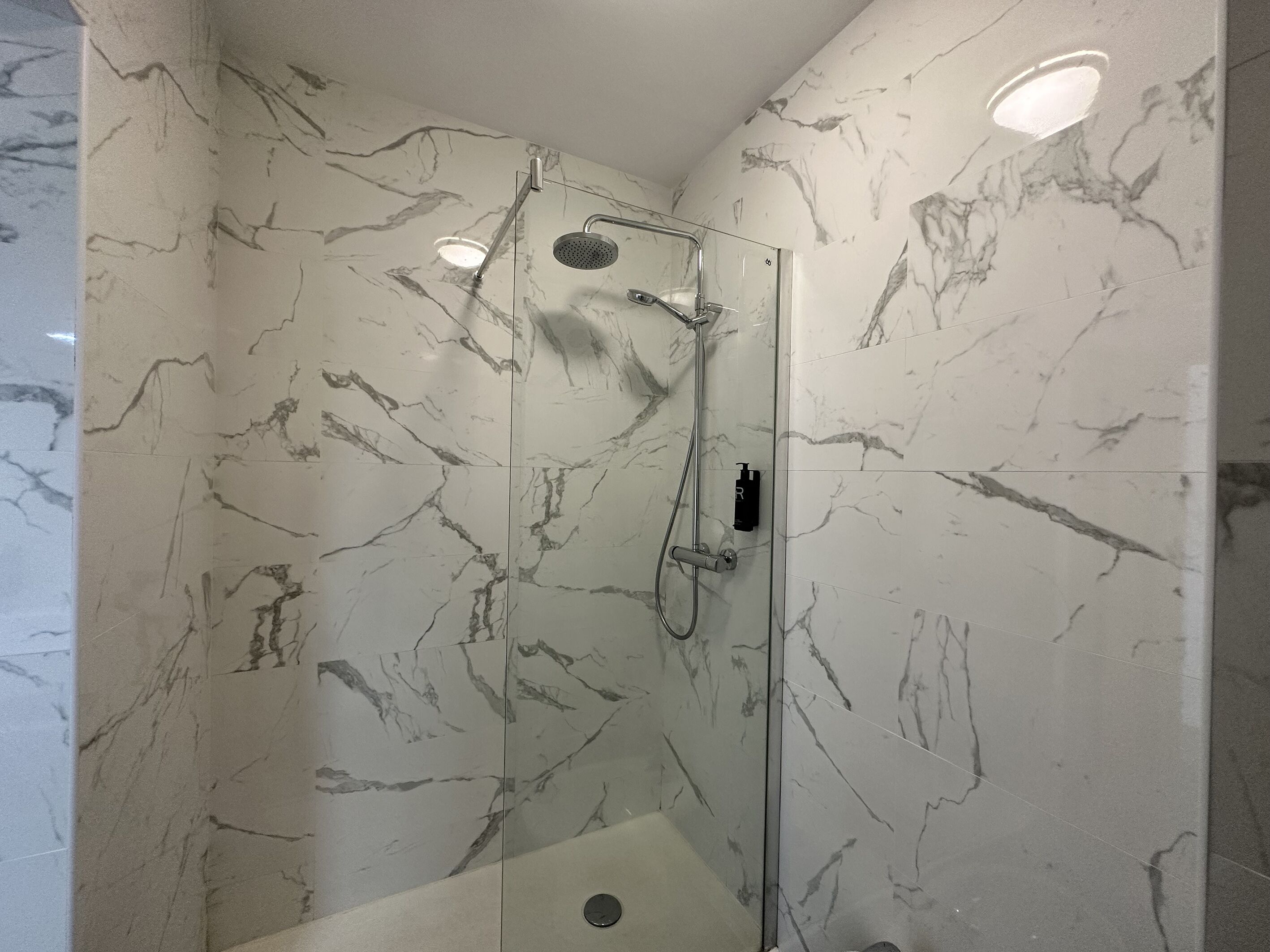 A glass-enclosed shower with a handheld showerhead and a wall-mounted faucet.