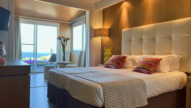 Une chambre d’hôtel moderne avec un grand lit, une vue sur l’océan et un balcon équipé d’une table et de chaises.