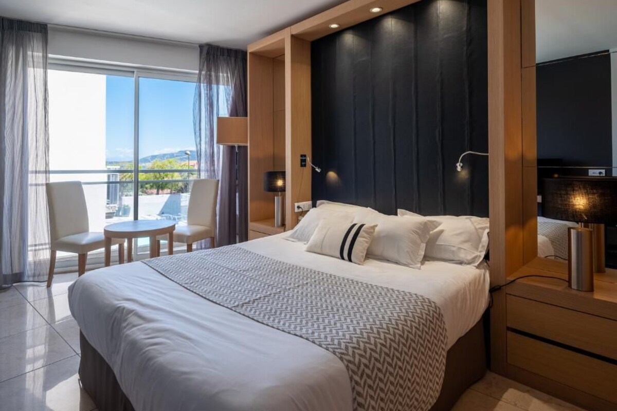 A hotel room with a large bed, a round table, and a balcony with a view.