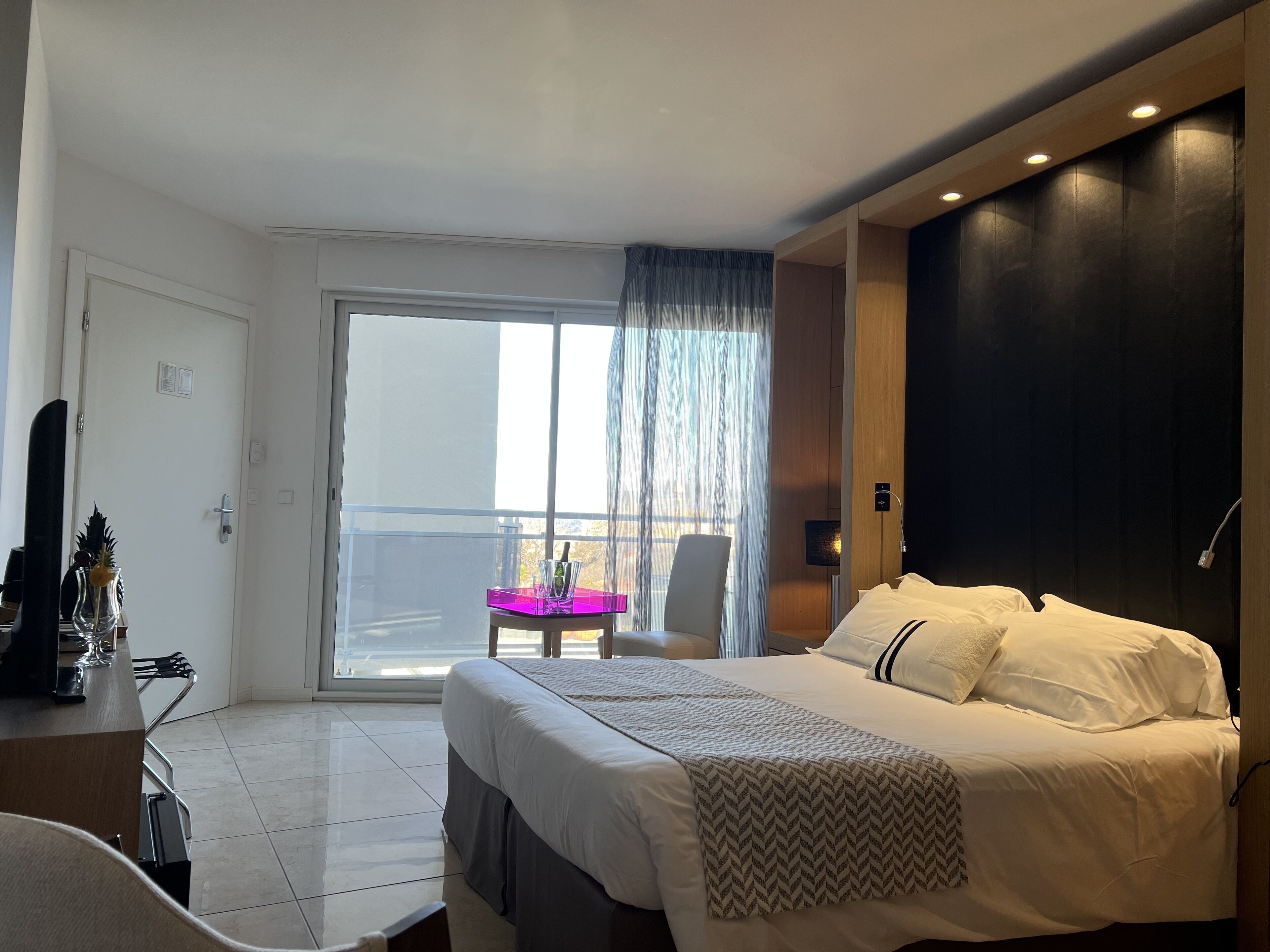Habitación de hotel con cama, escritorio, silla, balcón con mesa y vistas al exterior.