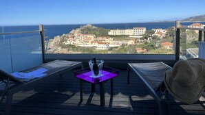 Un balcon donnant sur une ville côtière, une table avec un vase et une chaise.