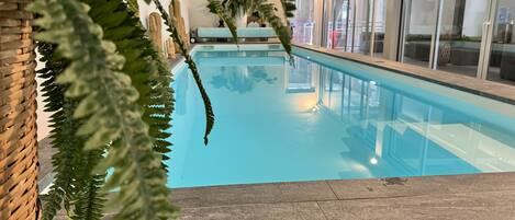 En swimmingpool med klart, blåt vand, omgivet af en stenterrasse og glasdøre.