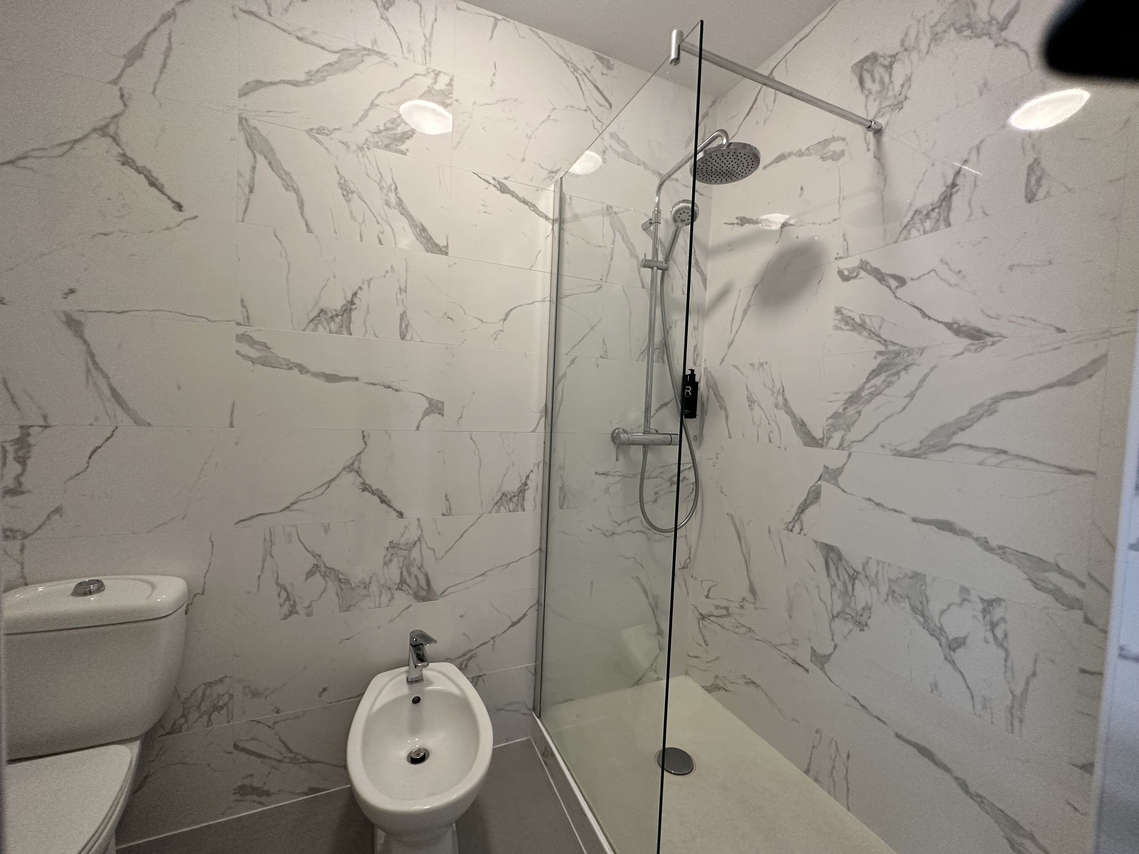 A bathroom with a marble wall, a toilet, a bidet, and a glass-enclosed shower area.