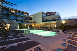 A hotel with a swimming pool, lounge chairs, and a multi-story building with balconies. - Hotel Revellata (Calvi)