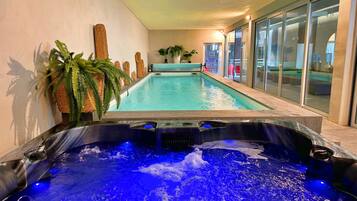 Une piscine avec un jacuzzi au premier plan, entourée de murs et de plantes en pot.