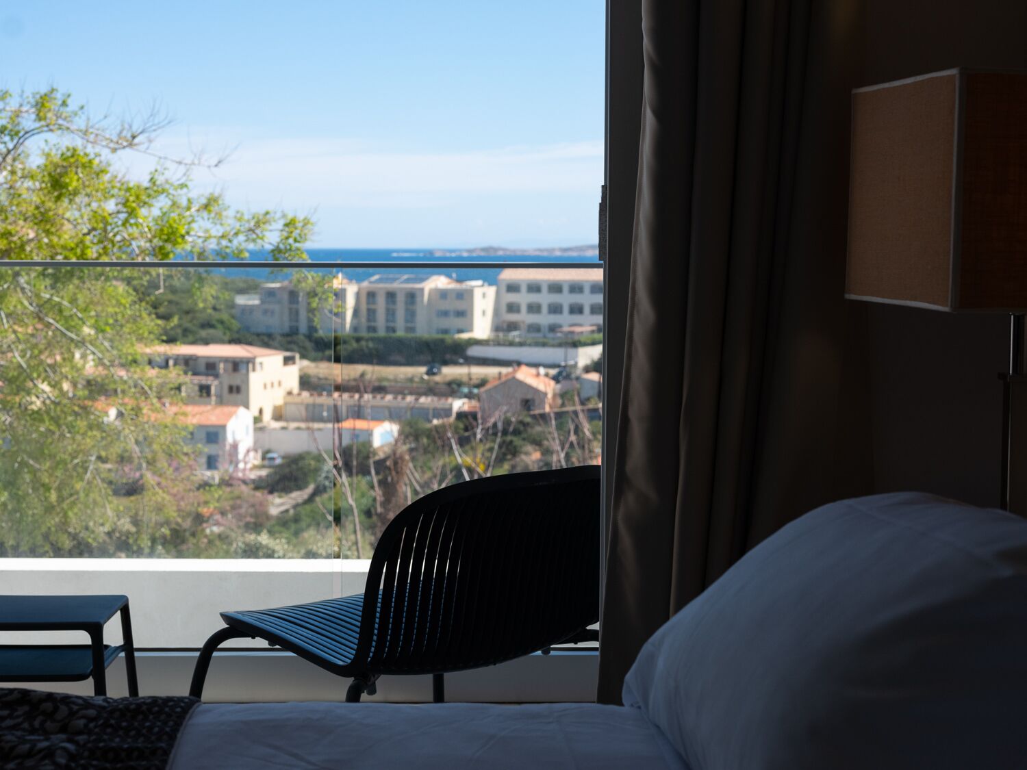 A hotel room with a bed, a chair, and a view of buildings and trees.