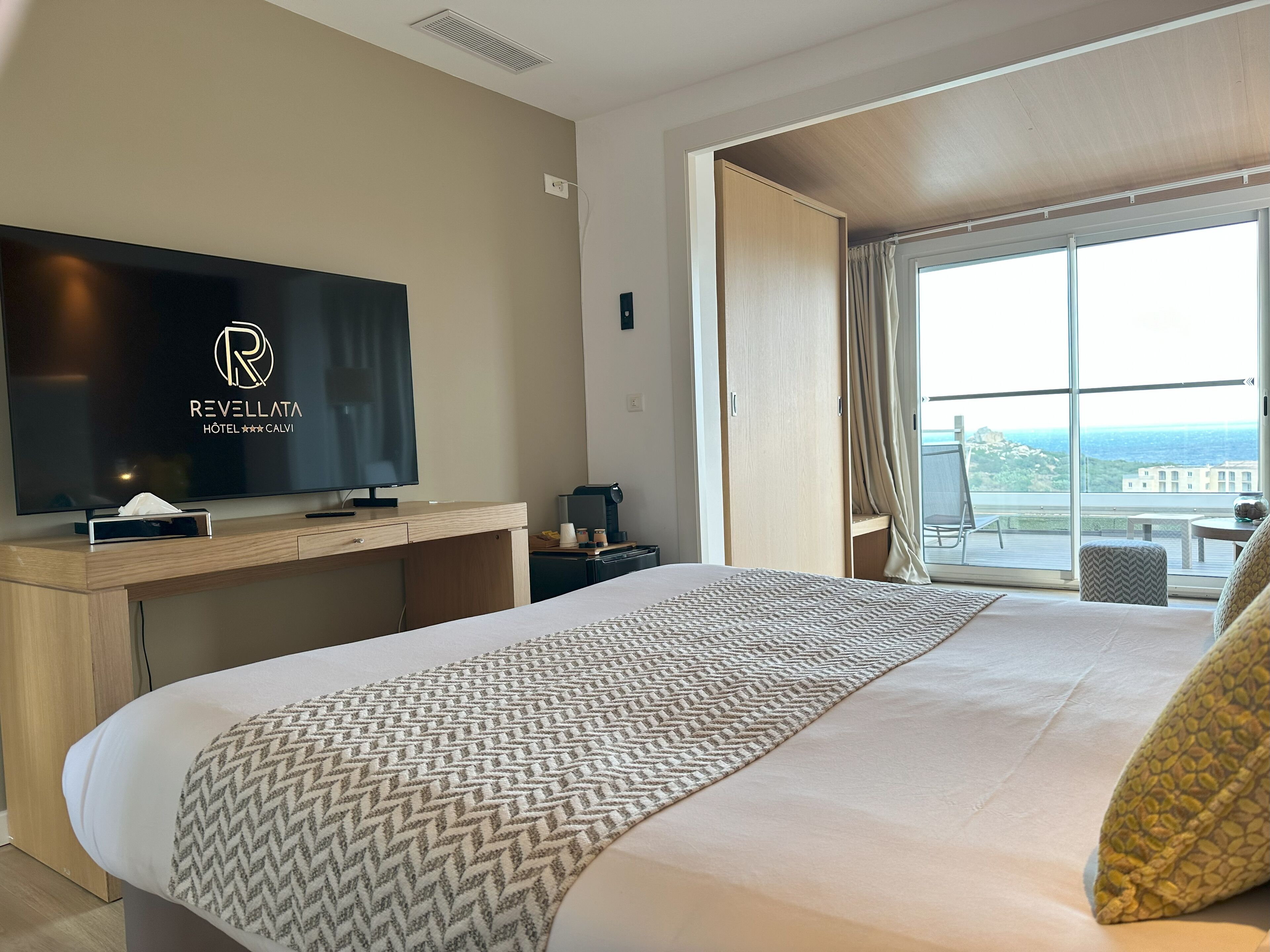 A hotel room with a bed, a TV, a desk, and a window with a view.
