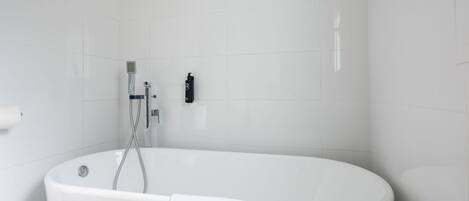 Une salle de bain moderne avec une baignoire sur pieds, une douchette et un flacon de shampoing fixé au mur.