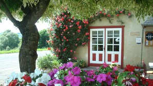 A building with a red door and windows, surrounded by a garden with pink and white flowers. - L'Auberge Basque (Ozon)
