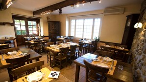 A restaurant with multiple wooden tables and chairs, arranged in a spacious dining area with large windows allowing natural light. - L'Auberge Basque (Ozon)