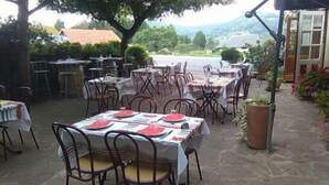 An outdoor dining area with tables and chairs, surrounded by greenery and a view of the countryside. - L'Auberge Basque (Ozon)
