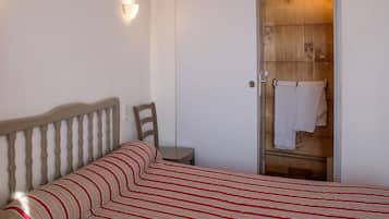 A bedroom with a bed, a chair, a bedside table, and a door leading to a bathroom.