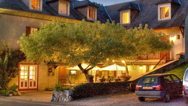 A two-story building with a tree in front, outdoor seating, and a car parked nearby. - L'Auberge Basque (Ozon)