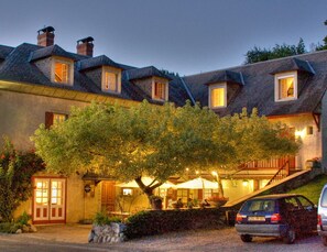 A two-story building with a tree in front, outdoor seating, and a car parked nearby.