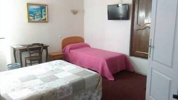 Um quarto pequeno com uma cama, uma escrivaninha, uma cadeira, uma televisão e uma porta.