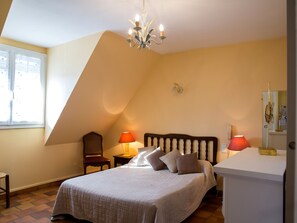 A bedroom with a sloped ceiling, a bed with a wooden headboard, two bedside lamps, a chair, and a small table.