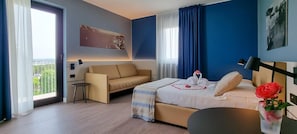 A hotel room with a bed, a sofa, a small table, and a view of the outdoors.