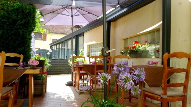 Un área de patio al aire libre con mesas y sillas de madera, cubierta por un gran paraguas.