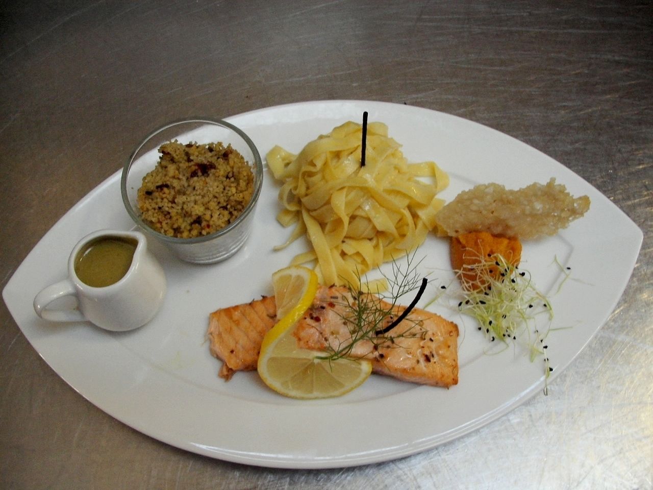 A plate with salmon, pasta, and a small bowl of sauce.