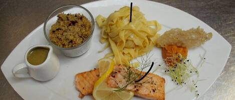 A plate with salmon, pasta, and a small bowl of sauce.