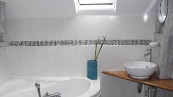 Un baño moderno con una bañera independiente, un lavabo con recipiente y un jarrón azul con follaje.