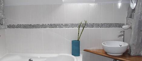A modern bathroom with a freestanding bathtub, a sink with a vessel basin, and a blue vase with greenery.