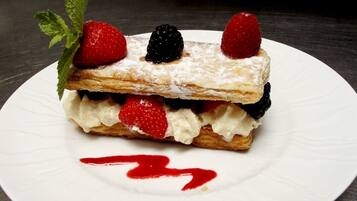 Postre en un plato blanco con fresas y frambuesas encima, espolvoreado con azúcar glas y salsa roja en el plato.