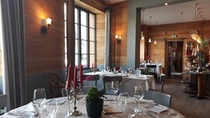 Un comedor con mesas dispuestas para una comida, paredes de madera y ventanas amplias.