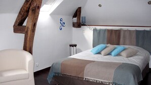 Un dormitorio con cama, una silla, una mesita y una ventana.