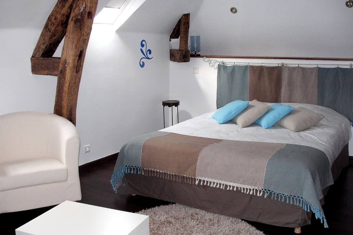 A bedroom with a bed, a chair, a small table, and a window.