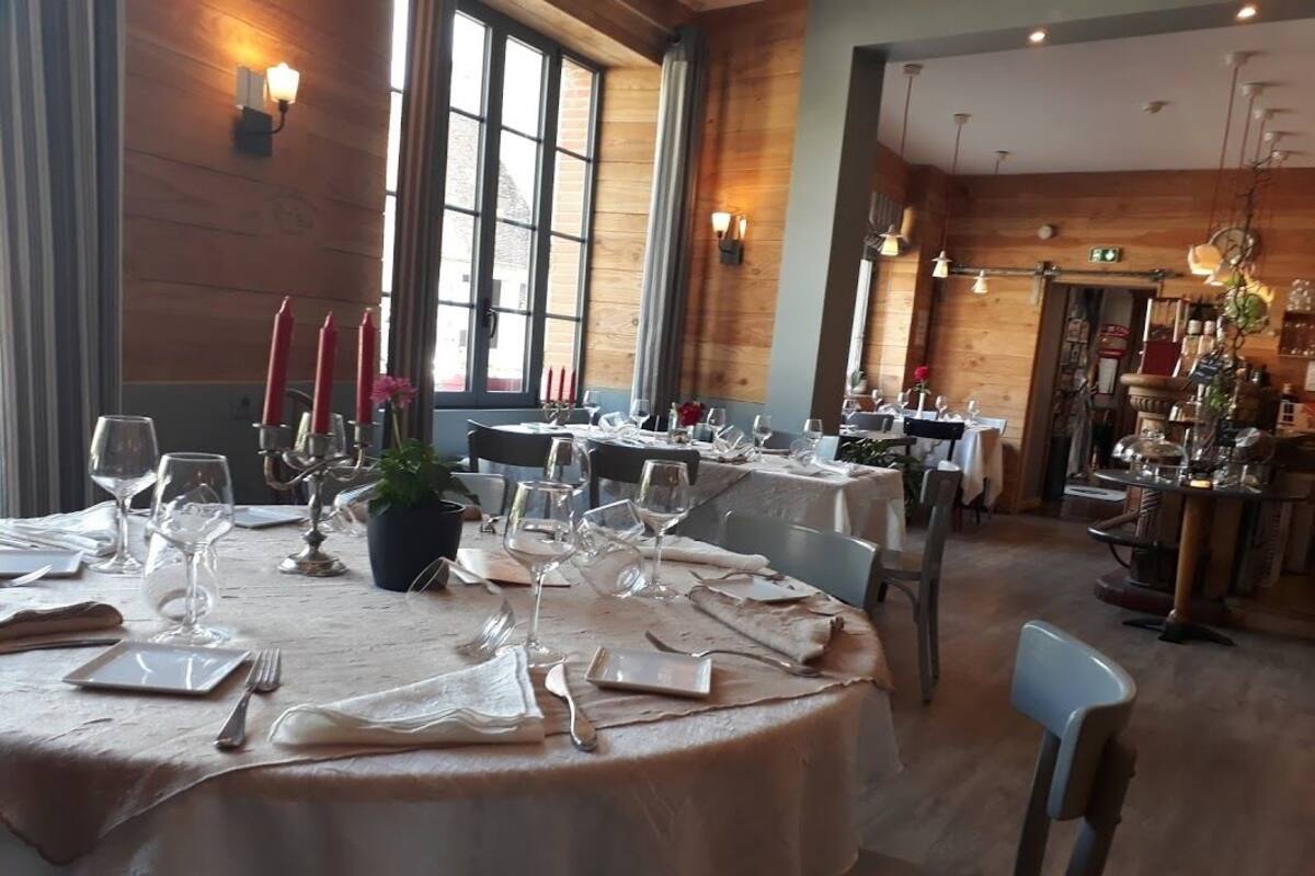 A restaurant with round tables set for dining, featuring candle holders, wine glasses, and a potted plant.