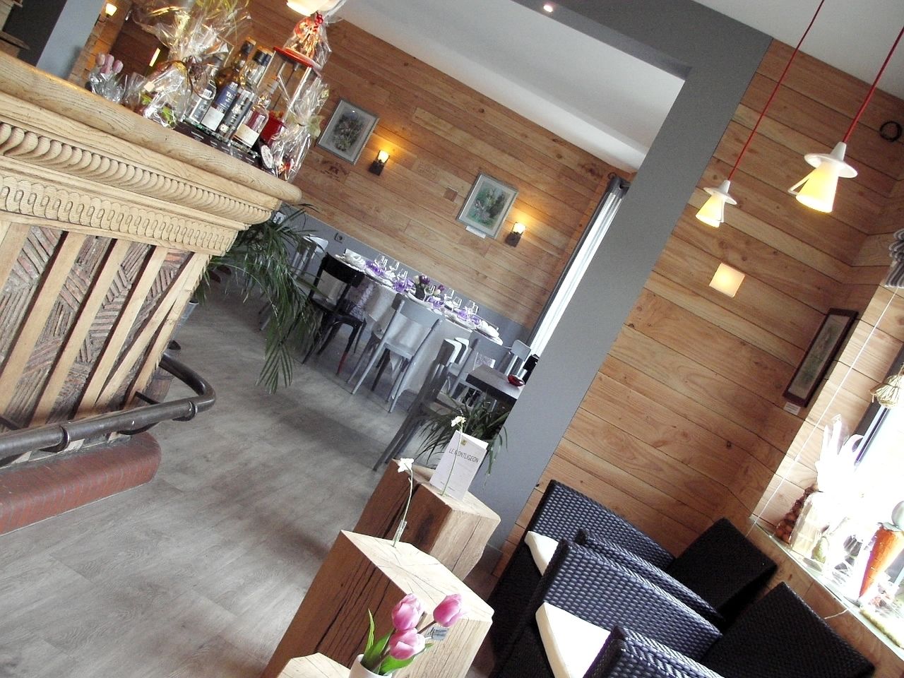 A restaurant with wooden walls, tables, chairs, and hanging pendant lights.
