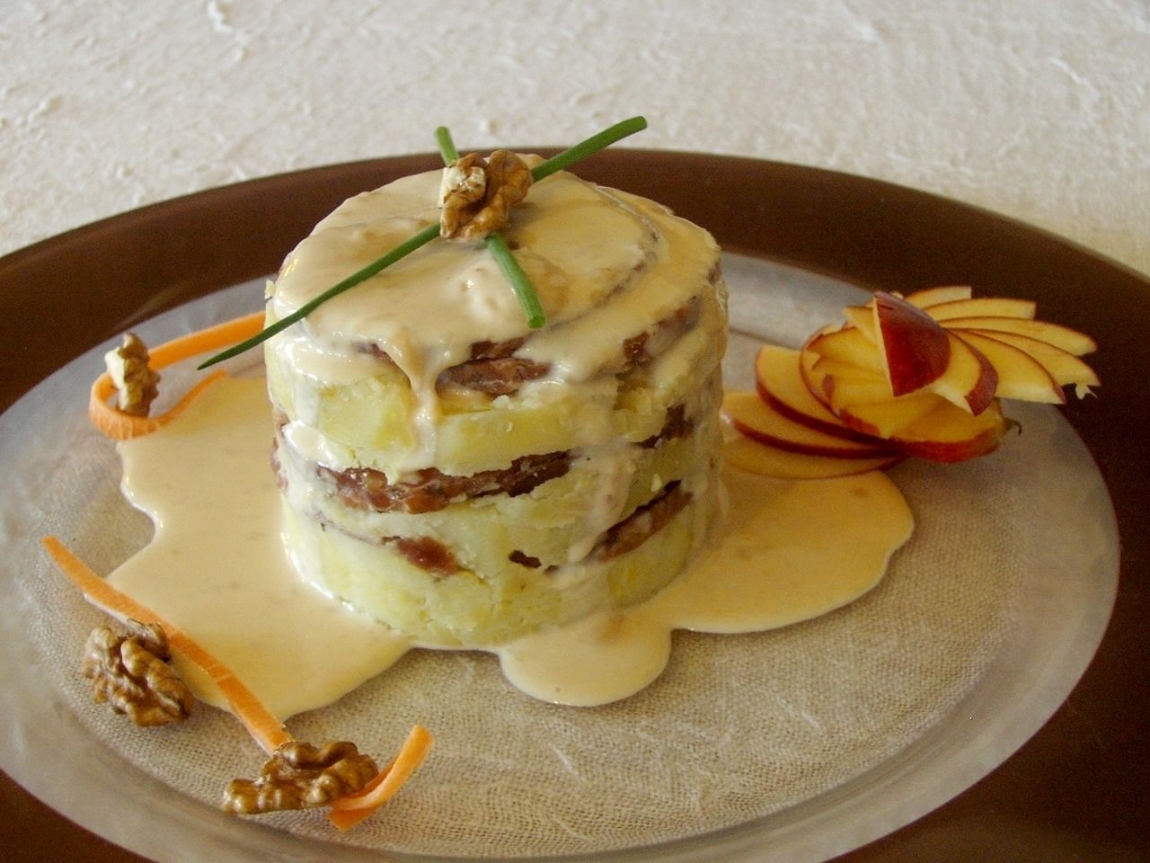 Un dessert composé de plusieurs couches, avec des noix et une sauce crémeuse, présenté dans une assiette.