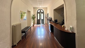 A hallway with a wooden floor, a reception desk, a bench, and a plant. -  Logis Hôtel des Thermes  (Lamalou-les-Bains)