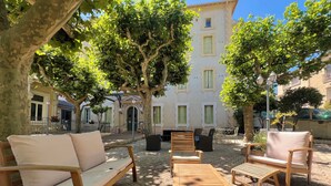 A courtyard with outdoor seating, including a sofa and chairs, surrounded by trees and a building with multiple windows.