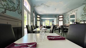 A dining area with tables set for two, featuring a white tablecloth, black chairs, and a red napkin with silverware. -  Logis Hôtel des Thermes  (Lamalou-les-Bains)