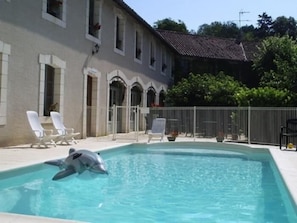 A swimming pool with a dolphin, surrounded by a building with arched windows and a tiled roof. - Hostellerie du Perigord Vert (Brantôme en Périgord)