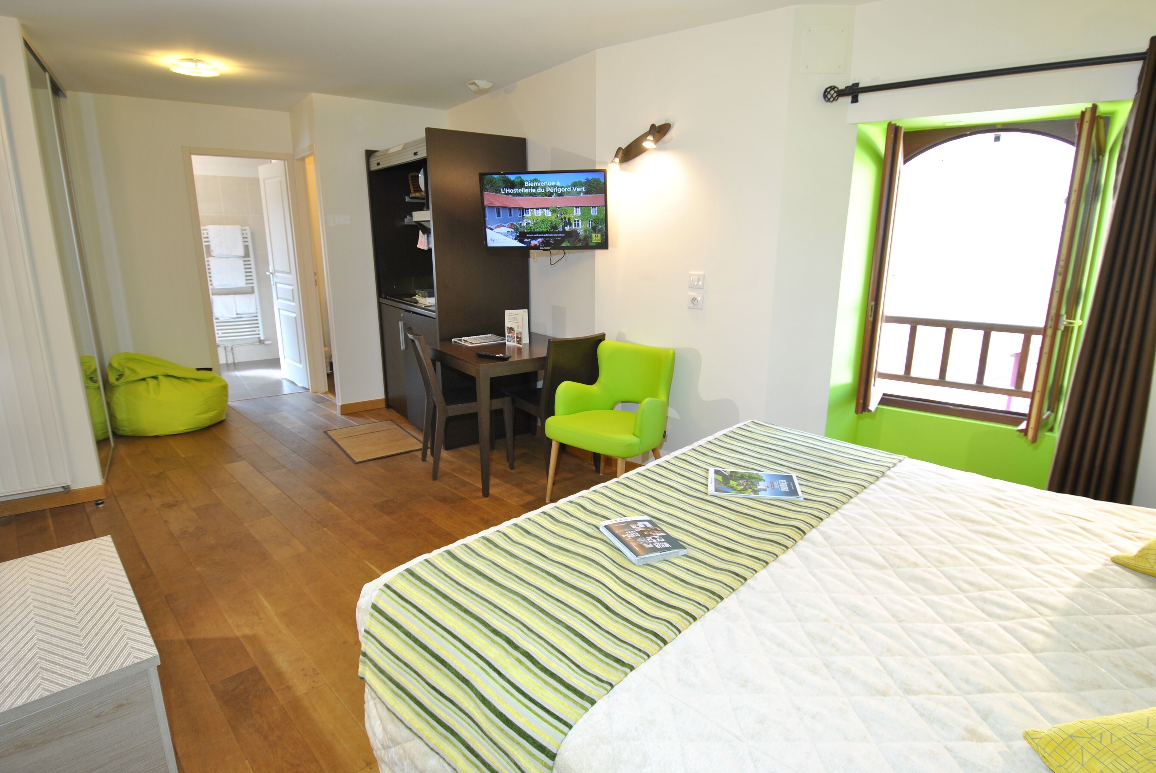 A hotel room with a bed, a desk, a chair, a TV, and a window with curtains.