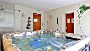 A spa room with a large hot tub, a wooden door, and a wall-mounted rock stack. - Hostellerie du Perigord Vert (Brantôme en Périgord)