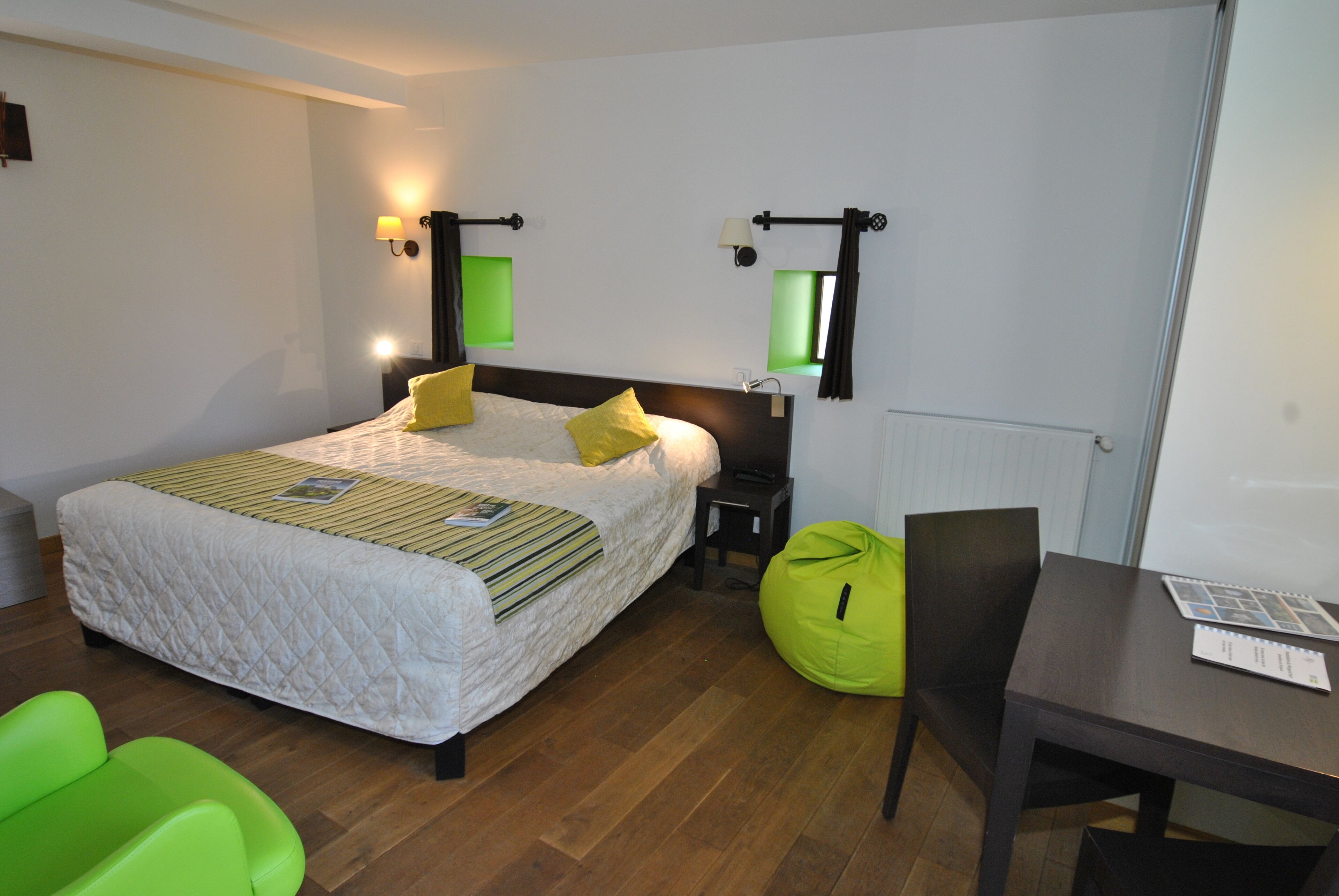 A hotel room with a bed, bedside tables, a desk, and a green bean bag chair.