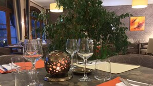 A dining table set with wine glasses, a decorative glass sphere, and orange placemats. - Hostellerie du Perigord Vert (Brantôme en Périgord)