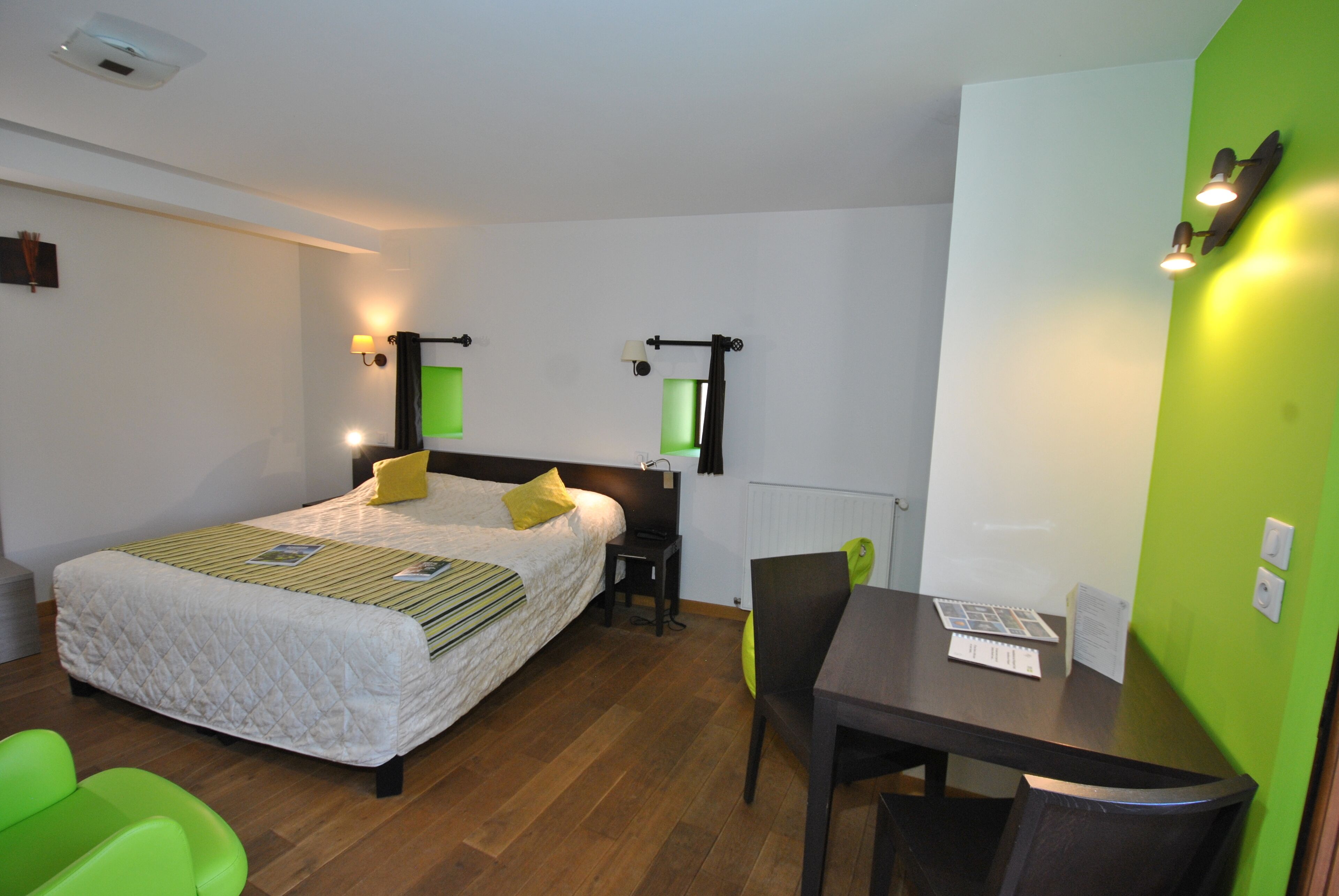 A hotel room with a bed, a desk, and a chair. There is a green wall and a white wall.