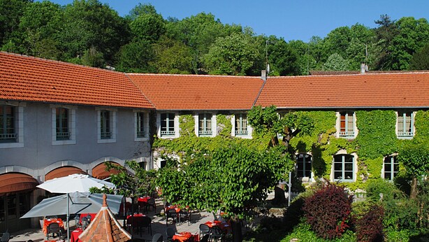 A courtyard with outdoor seating, a building with a red-tiled roof, and greenery. - Hostellerie du Perigord Vert (Brantôme en Périgord)