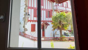 Una ventana con vista a un edificio tradicional de fachada roja y blanca, un balcón y una palmera.