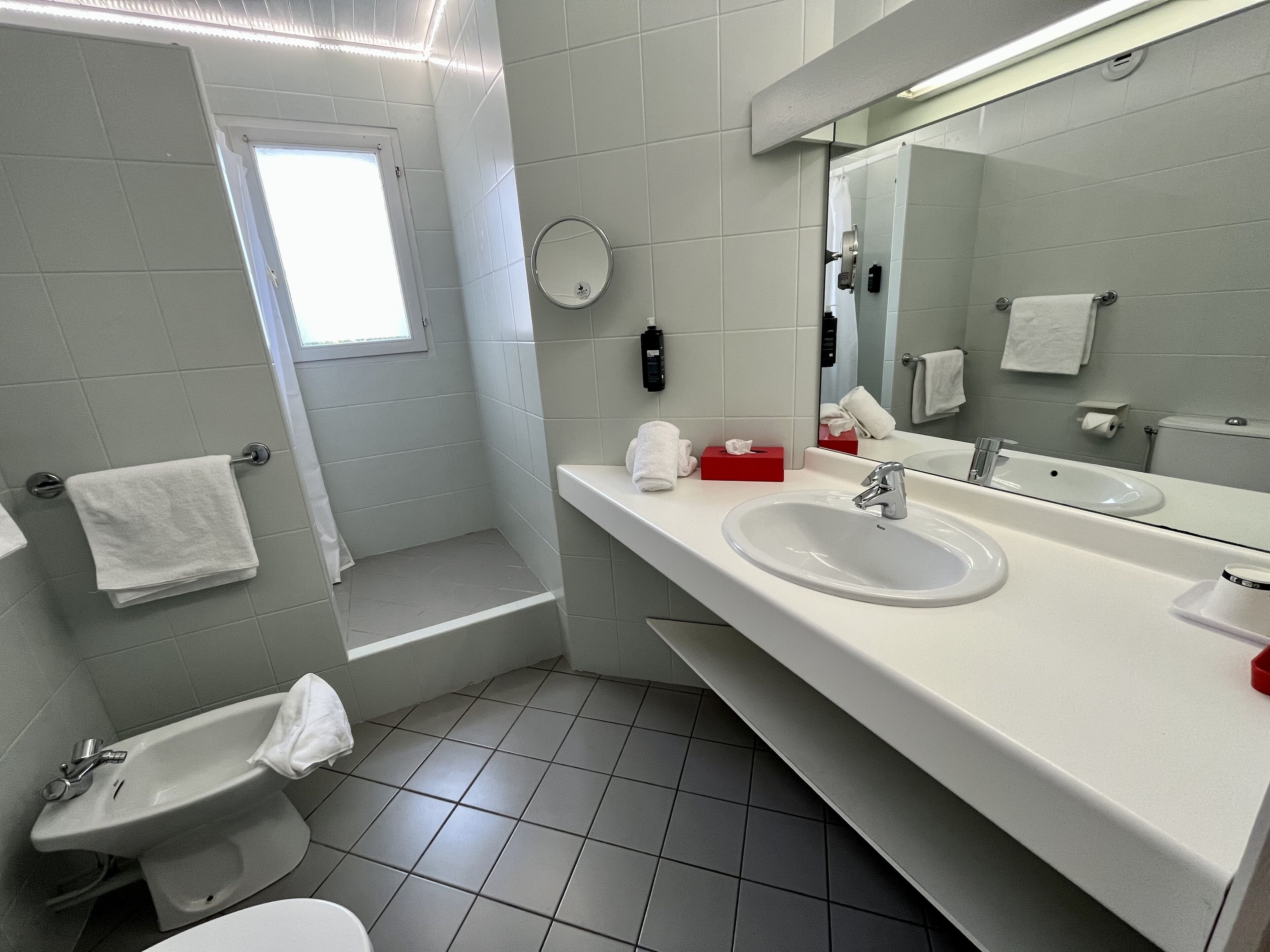 A modern bathroom with a white sink, mirror, and a small window.