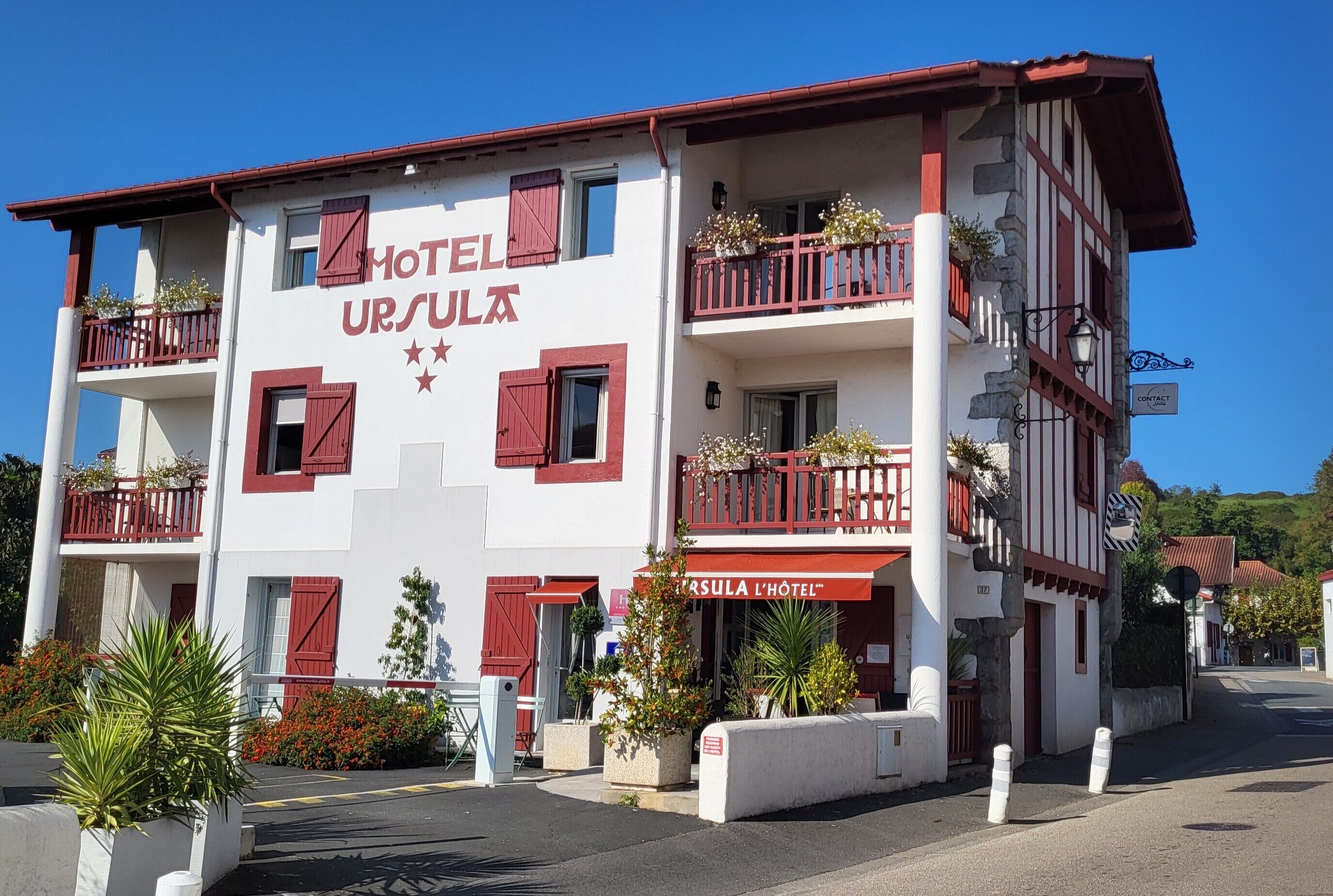 A two-story hotel with balconies, a sign reading 'HOTEL URSULA,' and a 'CONTACT' sign.