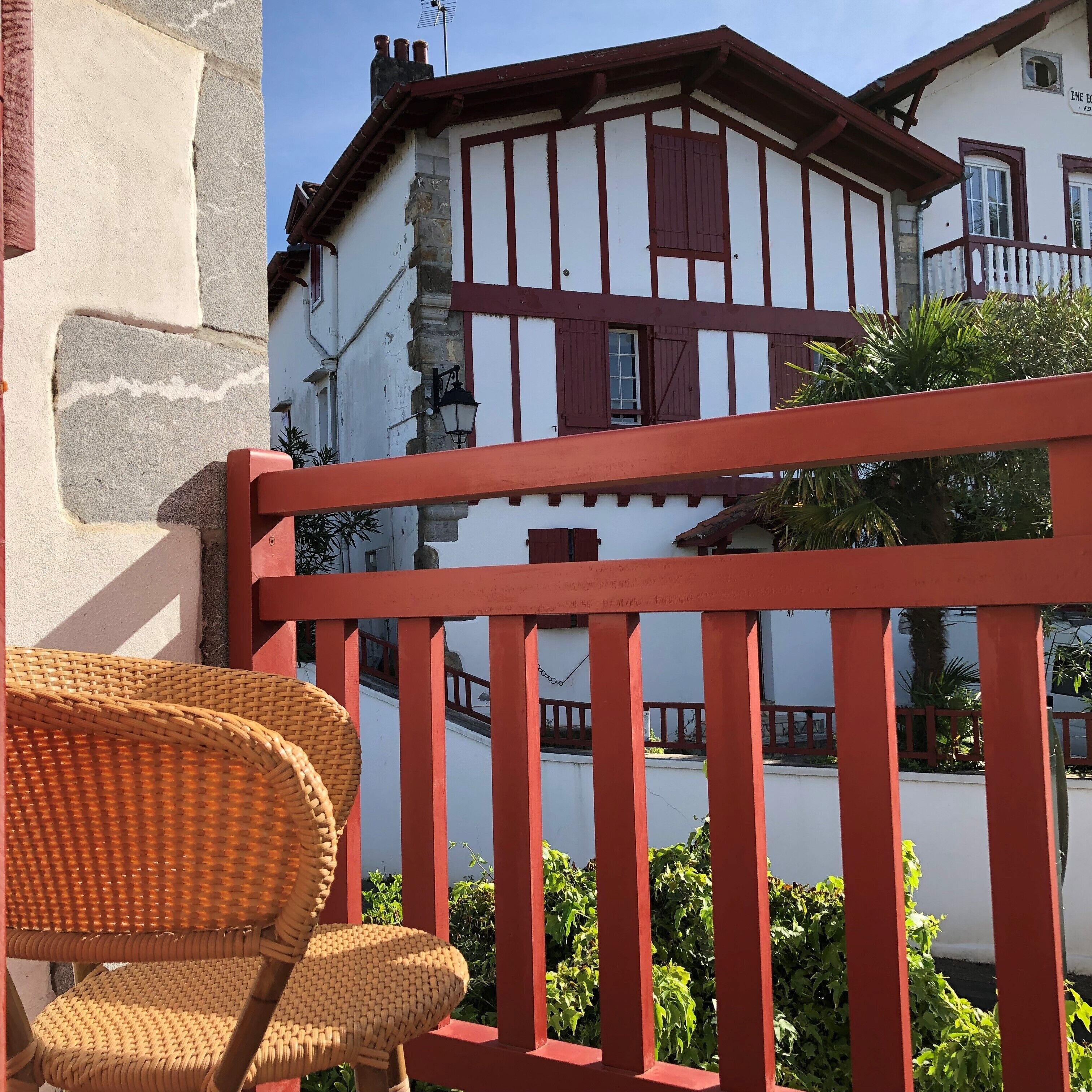A traditional building with a balcony, a wicker chair, and red railings.