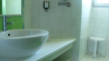 A bathroom with a white sink, green tiles, a mirror, a soap dispenser, a small trash bin, and a window.